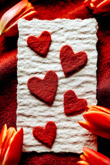 Red felt hearts on white handmade paper surrounded by orange tulip petals.