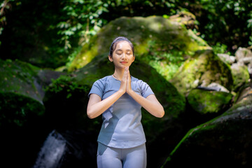 Asian woman enjoying yoga alone in nature with large mossy rocks and flowing river water in the forest