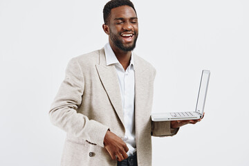 Smiling man wearing beige blazer and white shirt holding open laptop computer in hand, looking...