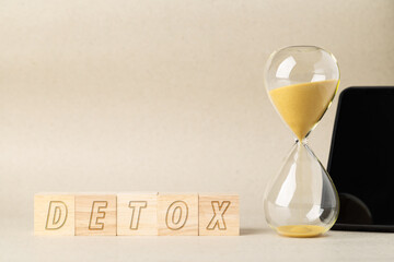 Wooden blocks spelling DETOX arranged with an hourglass and a blurred smartphone. A conceptual image for digital detox, screen time management, mental health awareness, and technology balance.