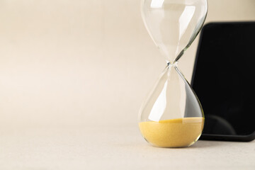 An hourglass with golden sand stands next to a blurred smartphone on a neutral background. Conceptual image representing digital detox, time management, screen time addiction, and mental wellness.