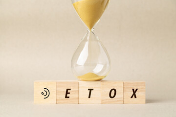Hourglass on wooden blocks spelling DETOX with a listening ear symbol. A conceptual image for digital detox, mindfulness, mental health awareness, and finding inner peace from technology noise.