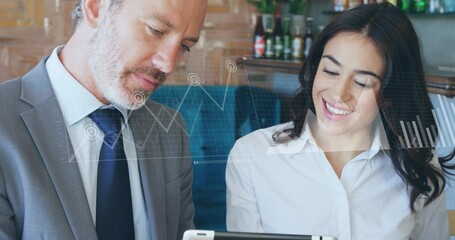 Reviewing two colleagues leaning over tablet at cafe, showing financial overlay in suit and blouse