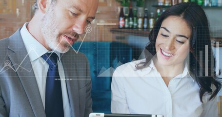 Discussing data, colleagues in suit and blouse leaning over tablet in bar, with chart overlays
