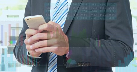 Holding phone, businessman in dark suit and striped tie at office window, with financial charts