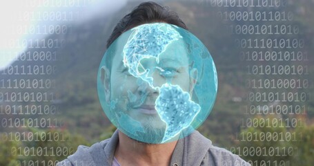 Standing man wearing gray hoodie facing camera on hillside, with digital globe and binary overlay