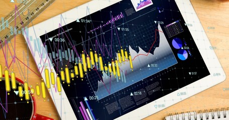 Displaying tablet showing dashboard with yellow candles and line graphs on desk, with red mug