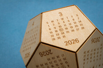 March 2026 - small wooden dodecahedron desktop calendar against art paper, time and business concept