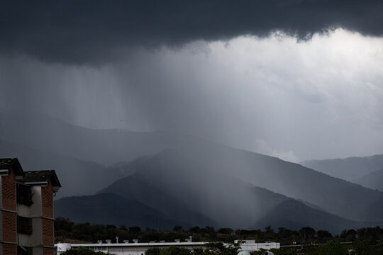 Heavy tropical rain curtain falling over mountain range under dark storm clouds