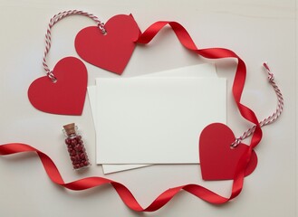Red heart tags, ribbon, blank cards, and candy jar arranged for Valentine's Day.