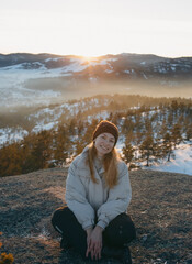 A girl sits on top of a mountain at sunset in winter