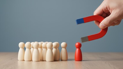 Hand holding magnet attracting a red figure from a group symbolizing team and target attraction