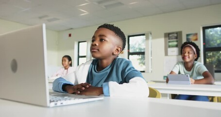 Camera zooming, African American students sitting at desks working on laptop and tablets for lesson - Powered by Adobe