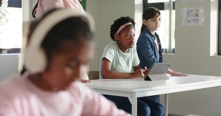 Diverse classroom focusing teacher nearing Indian teen girl pink top headset tapping tablet working - Powered by Adobe