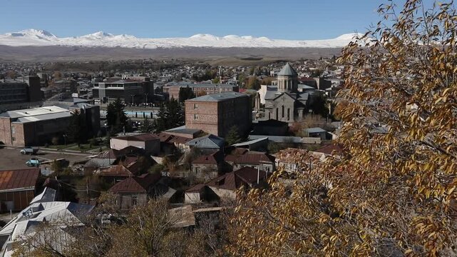 Panoramic view of Gyumri, Armenia, featuring traditional architecture. Majestic snow-capped peaks of Mount Aragats rise in the background under a clear blue sky during a sunny autumn day.


