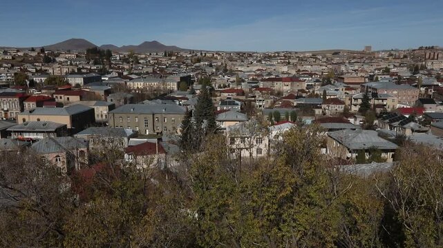 Panoramic view of Gyumri, Armenia, featuring traditional architecture. Majestic snow-capped peaks of Mount Aragats rise in the background under a clear blue sky during a sunny autumn day.

