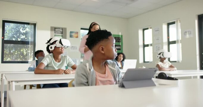 Teenage African American male at desk glancing as teacher approaching checking tablet tapping folio