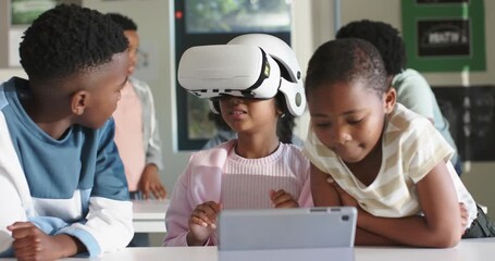 African American child after tech lesson putting on white VR headset at desk peers watching tablet - Powered by Adobe