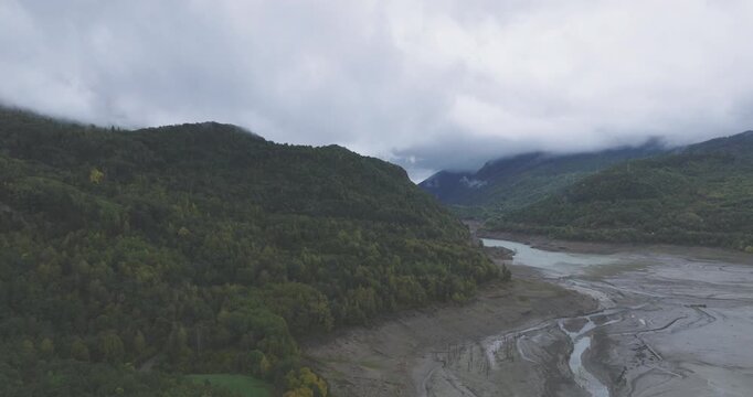 Drone aerial across misty Pyrenees valley near Huelva, Spain and France, braided river channels and forested slopes under heavy overcast skies