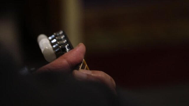 Close up shot of a musician's hand adjusting the tuning pegs on the headstock of an acoustic guitar to correct the pitch before a musical performance.

