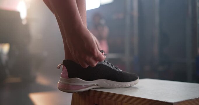 Athlete's hands are reaching down, threading, tightening black laces on box, preparing for workout