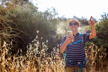 Teenage boy hiking in summer while checking his phone for navigation. Modern outdoor lifestyle combining technology, travel, and exploration in nature.