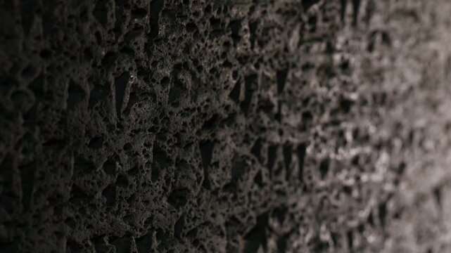 Extreme close-up vertical panning shot of an ancient dark basalt stone surface with carved Hebrew inscriptions, revealing the rough texture and historical detail of this archaeological artifact.

