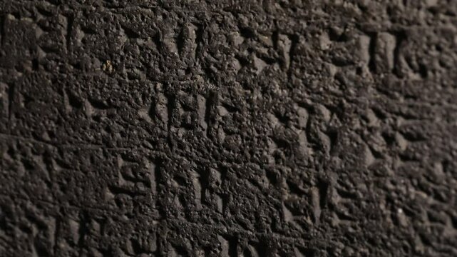 Extreme close-up vertical panning shot of an ancient dark basalt stone surface with carved Hebrew inscriptions, revealing the rough texture and historical detail of this archaeological artifact.

