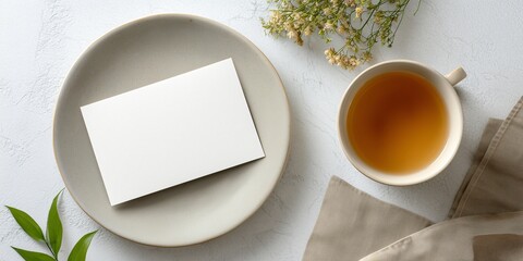 Overhead shot of a blank postcard mockup placed on a simple, white plate. A single, beautifully crafted cup of clear tea is nearby