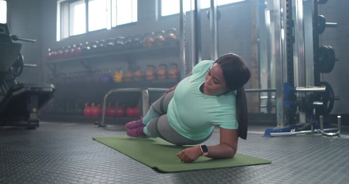 African American mid adult woman starting left forearm plank rolling prone toning core on gym mat