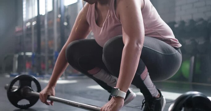 Female lifter in gym is clapping chalk dust gripping barbell lifting to hips bracing next rep