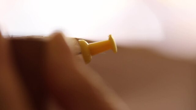 Macro shot of human fingers pulling out a yellow push pin and pushing a white thumbtack into a wooden surface, highlighting organization and attention to detail.


