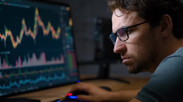 Medium shot of an economist examining cyclical price fluctuation charts with peaks and troughs on a computer screen during a research session.