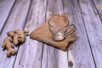 Empty glass tea cup on a dark stone, surrounded by lemon slices, fresh ginger and mint on a rustic wooden table. Natural light and zen-inspired composition