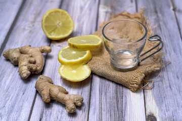 Empty glass tea cup on a dark stone, surrounded by lemon slices, fresh ginger and mint on a rustic wooden table. Natural light and zen-inspired composition