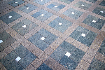 Geometric stone pavement pattern with square tiles arranged diagonally creating urban walkway texture with neutral tones and structured rhythm mood of order and durability