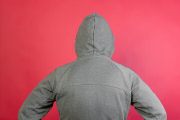 Man wearing a gray hoodie, standing with his back on red background