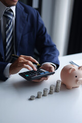 A person using a calculator with a piggy bank, stacks of coins, and US dollar bills on a table. Concept of saving money and financial planning.