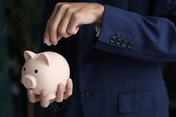 Businessman wearing suit putting a coin into a piggy bank. Saving money and financial planning, financial growth, investment, and future planning concept.