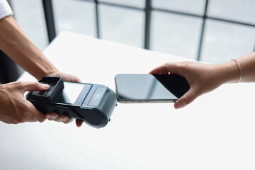 Copped hands of people using a smartphone to pay by holding close to a point-of-sale (POS) terminal. Contactless payment transaction is a fast and secure way to pay.