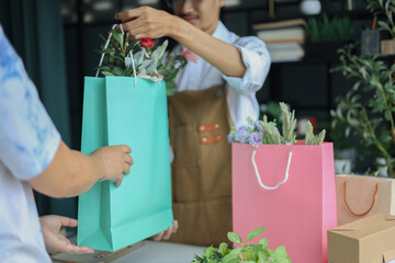 A florist or shop owner, handing a paper bag containing flowers to a customer.&nbsp;Flower shop, small business, retailing concept.