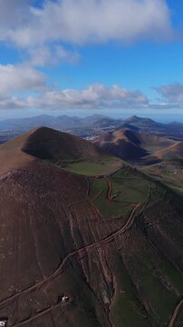 Vertical aerial shot over Lanzarote cones and craters, La Geria vineyards, dirt tracks, Atlantic coast, white towns. Bright daylight, scattered clouds, gentle glide.