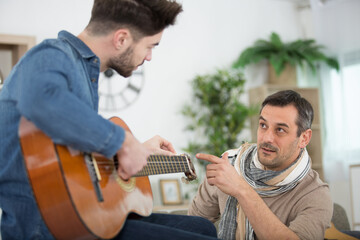 handsome man teaching son to play acoustic guitar at home