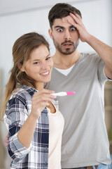 man is shocked as happy woman shows pregnancy test result