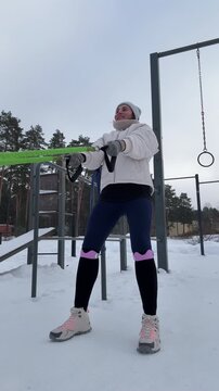 Woman Performing Resistance Band Squats at Outdoor Gym in Winter, Cold Weather Functional Training and Strength Endurance Concep
