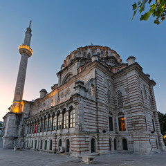 Fototapeta premium Laleli Mosque, or Laleli Camii, a historic Ottoman imperial mosque, illuminated at dusk in Istanbul, Turkey. Features its grand dome, minaret, and unique striped facade under a clear sky.