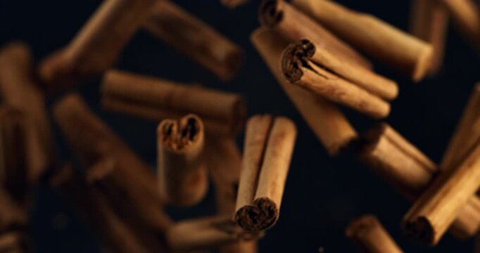 Slow Motion Macro Close Up Of Cinnamon Sticks Floating And Falling In Air With Warm Light And Cinematic Depth. Concept Of Spice, Aroma, Cozy Winter Mood