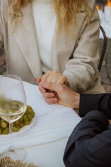 Obraz premium Romantic marriage proposal moment at outdoor cafe with couple holding hands, engagement ring, white wine and grapes. Intimate wedding or engagement scene with elegant table setting and warm atmosphere