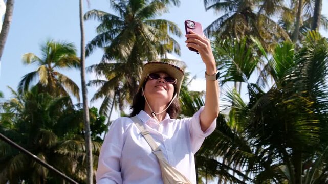 A young female tourist takes a selfie in front of the Dondra lighthouse and palm trees. A popular tourist destination in the south of Sri Lanka.