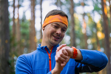 Smiling man in athletic gear viewing performance metrics on his wearable device while performing a...